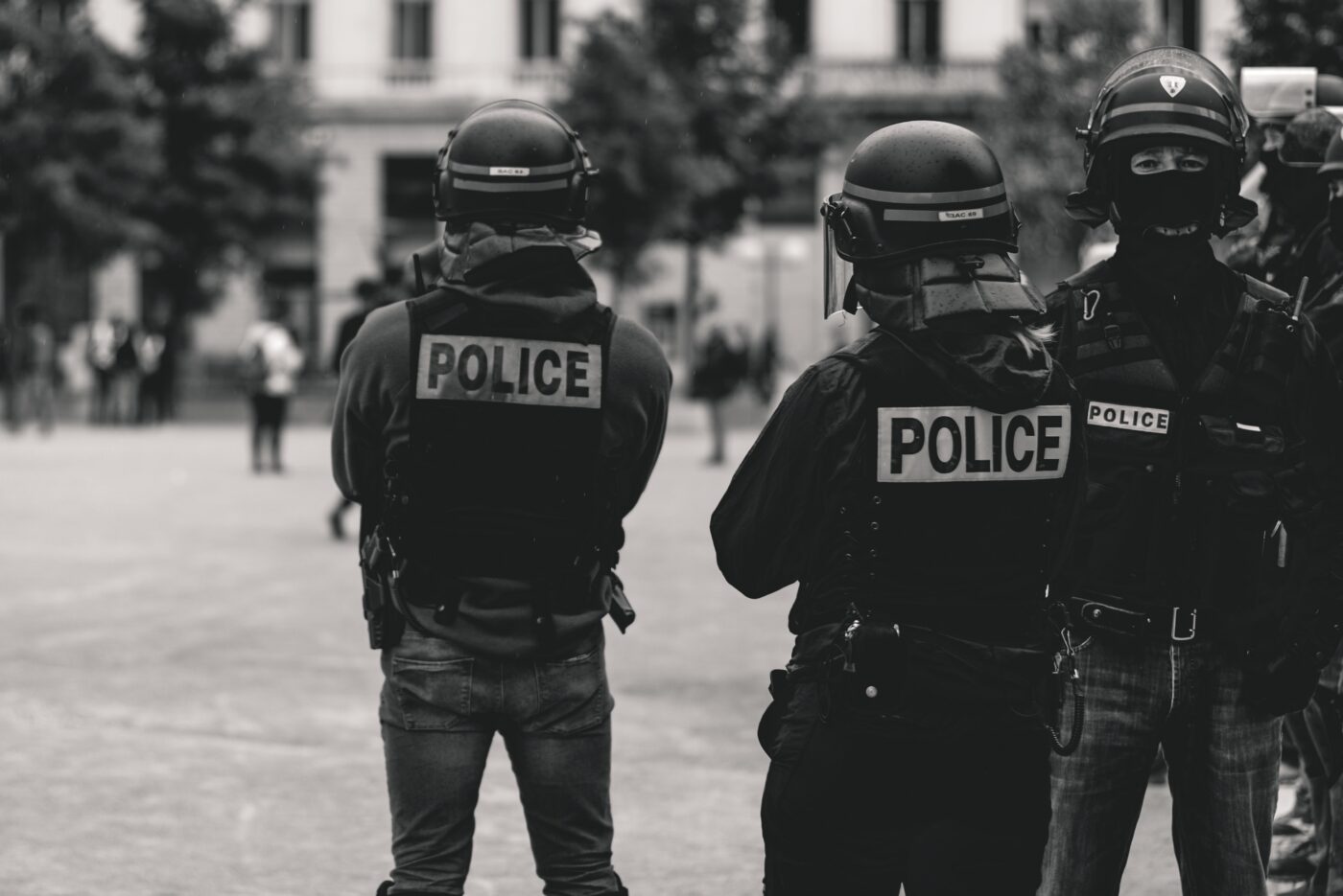 Duas pessoas de costas para a câmera vestem uniforme de polícia com a indicação "police", palavra inglesa para polícia