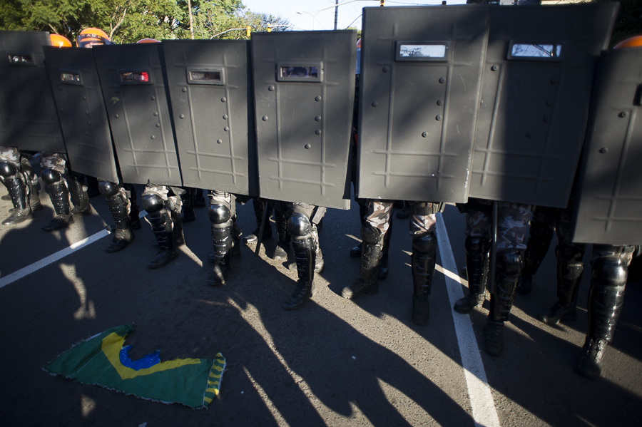 Barreira policial feita com escudos. No chão, há uma bandeira do Brasil rasgada