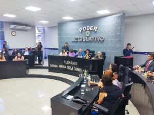 Pessoas estão em sentadas diante de bancadas em audiência pública. Na parede, está escrito Câmara Legislativa